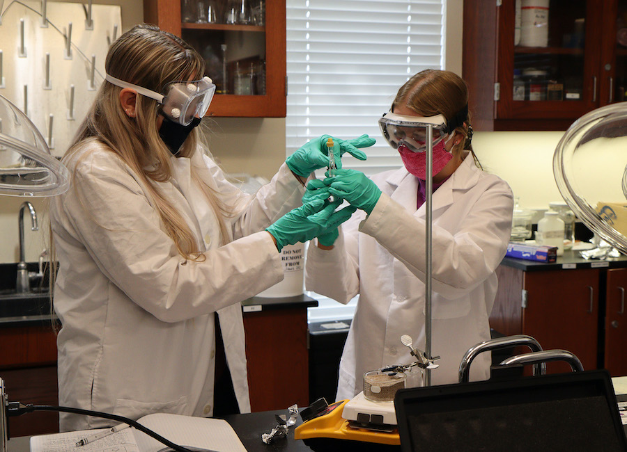 two students wearing lab coats and goggles 