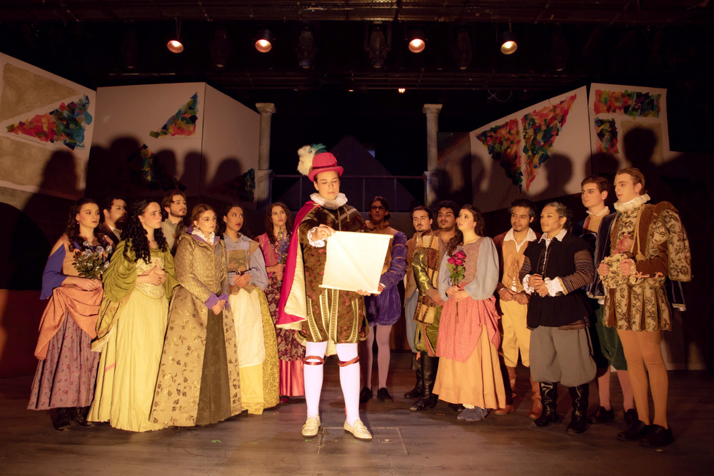 Group of actors on stage while one reads from a paper