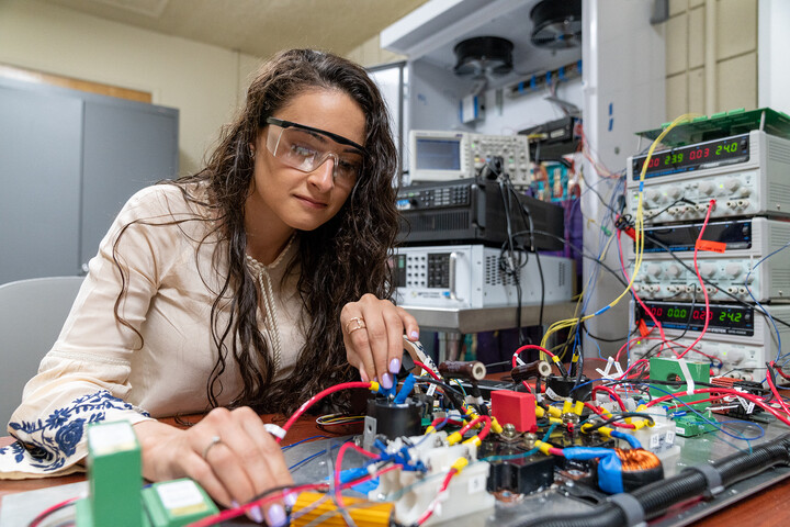 Student wearing safety goggles holding wires at a circuit board