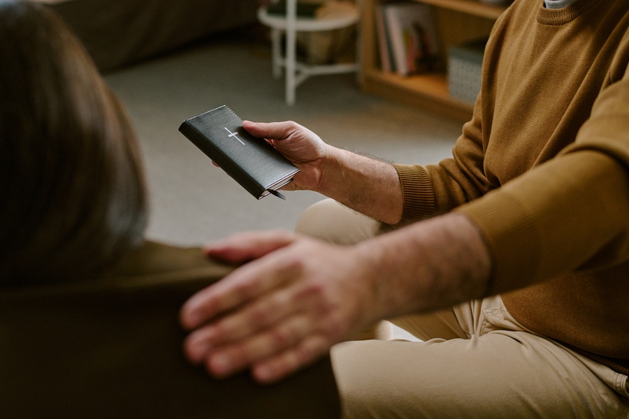 2 individuals with one comforting the other with a bible in their hand