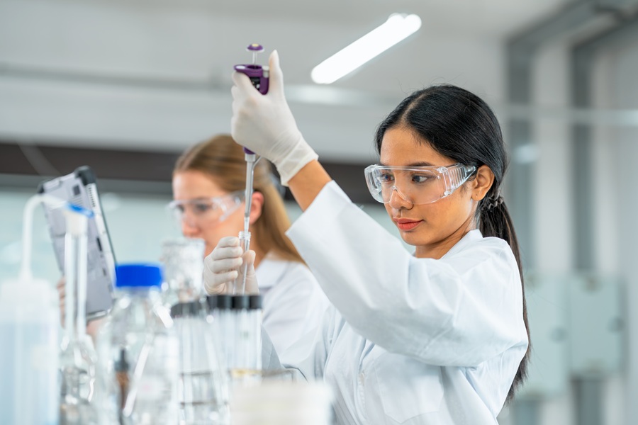 2 women doing a lab experiment with a monitor and several beakers on the table