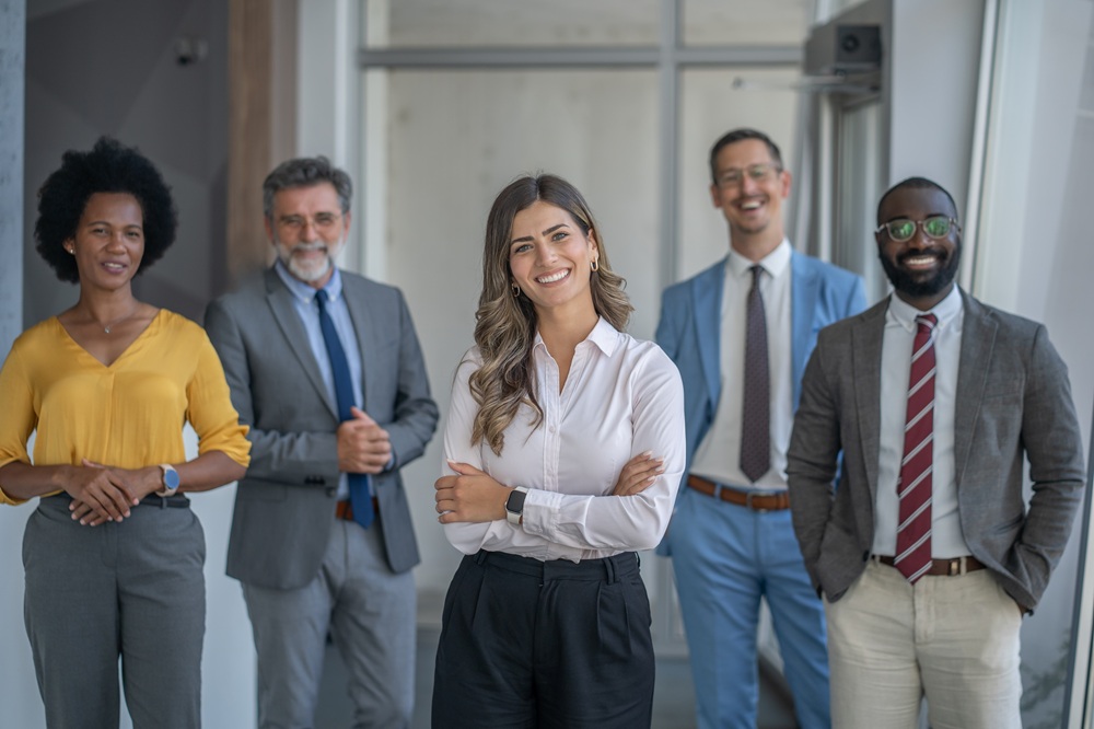 5 individuals smiling for the camera in professional outfits