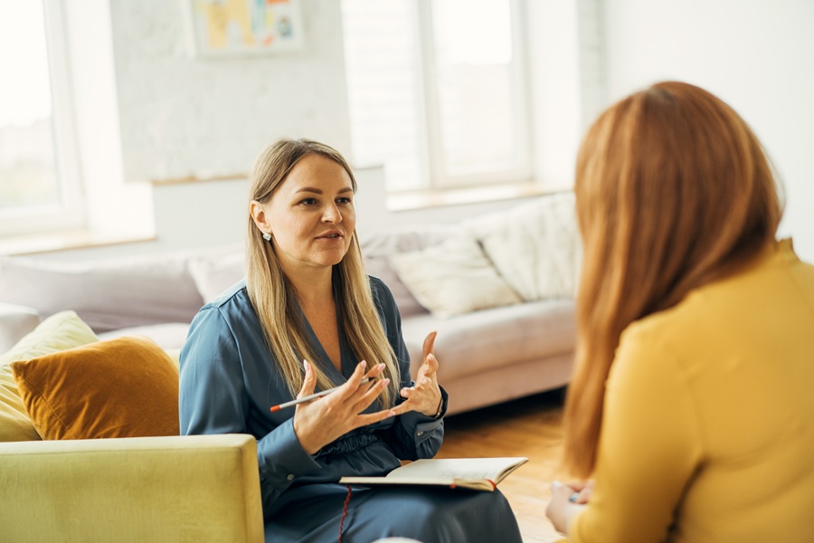 2 women talking on coaches while holding a notebook and pencil
